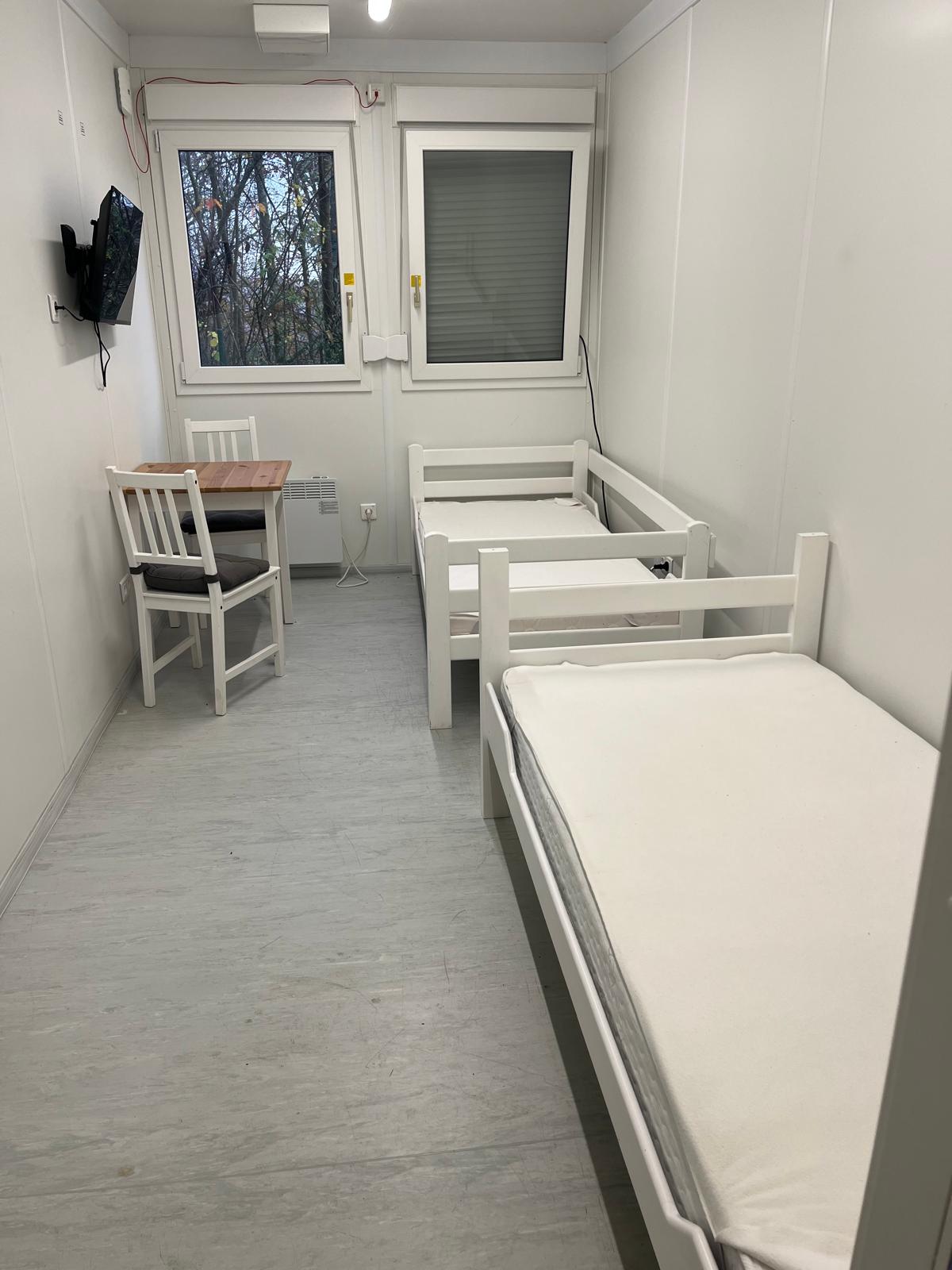 Möbliertes Zimmer mit Betten, Tisch und Fernseher